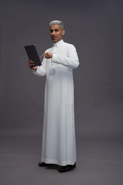 A portrait of an Arab Saudi Gulf man wearing a white thobe holding a mobile tablet in his hand, with various gestures and expressions, full body, gray background.