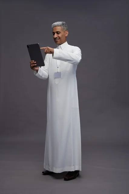 A portrait of an Arab Saudi Gulf man wearing a white thobe holding a mobile tablet in his hand, with various gestures and expressions, full body, gray background.