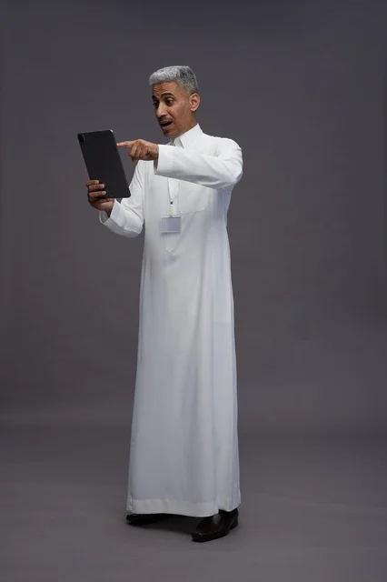 A portrait of an Arab Saudi Gulf man wearing a white thobe holding a mobile tablet in his hand, with various gestures and expressions, full body, gray background.
