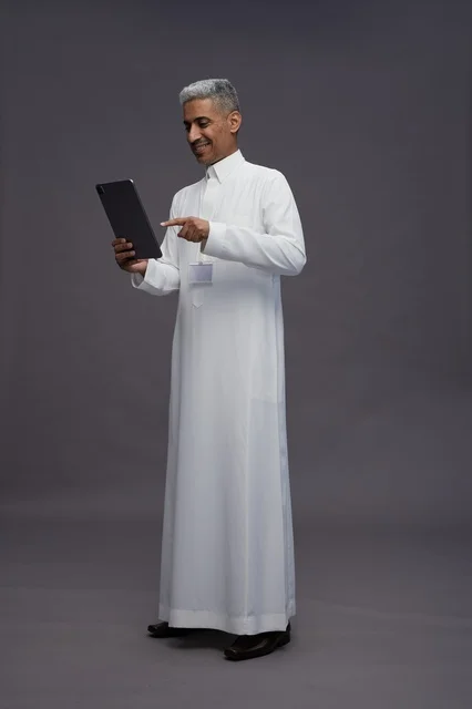 A portrait of an Arab Saudi Gulf man wearing a white thobe holding a mobile tablet in his hand, with various gestures and expressions, full body, gray background.