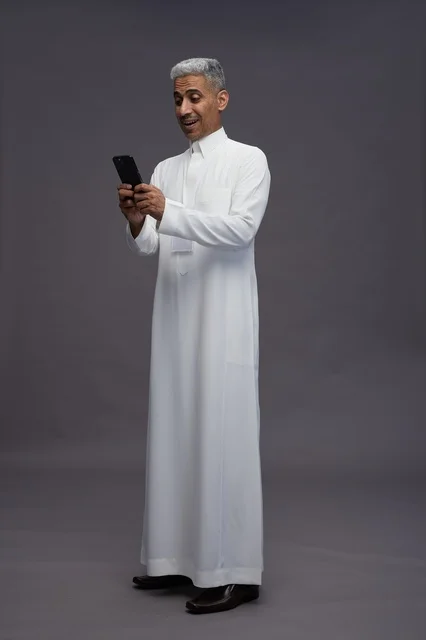 A portrait of an Arab Saudi Gulf man wearing a white thobe using a mobile phone, with various gestures and expressions, full body, gray background.