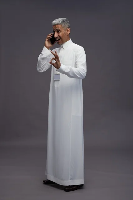 A portrait of an Arab Saudi Gulf man wearing a white thobe using a mobile phone, with various gestures and expressions, full body, gray background.