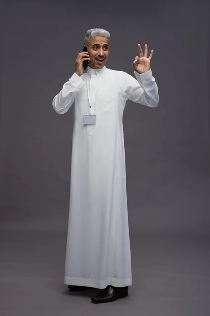 A portrait of an Arab Saudi Gulf man wearing a white thobe using a mobile phone, with various gestures and expressions, full body, gray background.