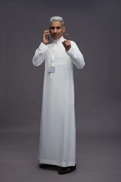 بورتريه لرجل عربي سعودي خليجي يرتدي الثوب الابيض يستخدم الهاتف المحمول, ايماءات وتعابير مختلفه, كامل الجسم, خلفيه رماديه