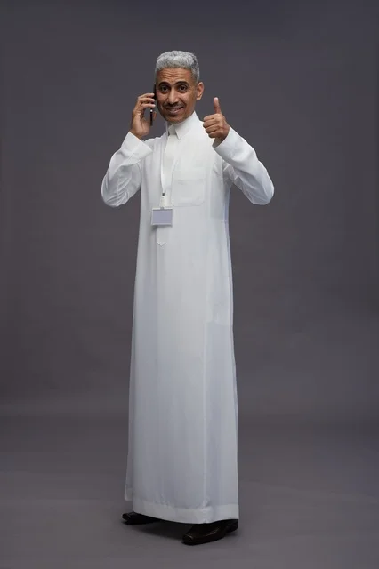 بورتريه لرجل عربي سعودي خليجي يرتدي الثوب الابيض يستخدم الهاتف المحمول, ايماءات وتعابير مختلفه, كامل الجسم, خلفيه رماديه