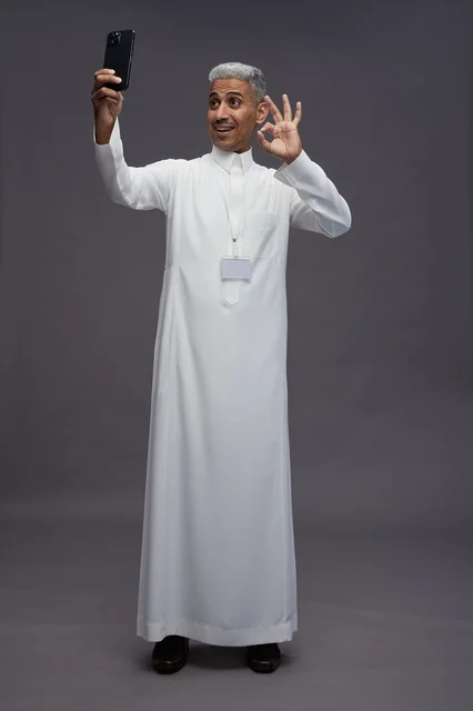 A portrait of an Arab Saudi Gulf man wearing a white thobe using a mobile phone, with various gestures and expressions, full body, gray background.