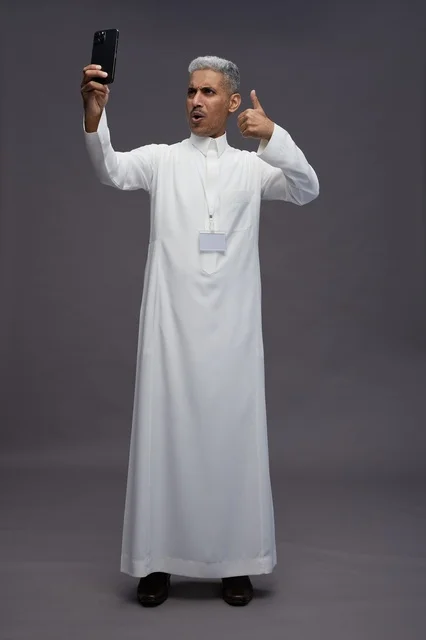 A portrait of an Arab Saudi Gulf man wearing a white thobe using a mobile phone, with various gestures and expressions, full body, gray background.