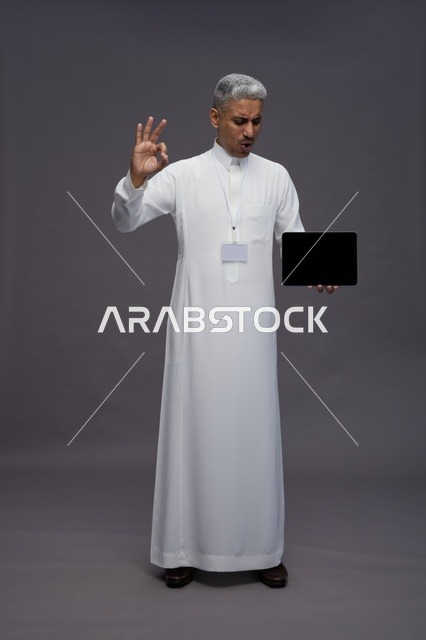 رجل سعودي يعرض جهازًا لوحيًا بشاشة فارغة