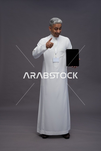 رجل سعودي يعرض جهازًا لوحيًا بشاشة فارغة