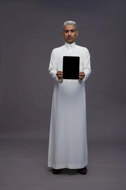رجل سعودي يعرض جهازًا لوحيًا بشاشة فارغة