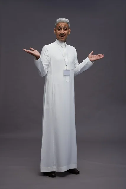 بورتريه لرجل عربي سعودي  خليجي يرتدي الثوب الابيض يقف و يقوم بايماءات واشارات مختلفه امام الكاميرا, خلفيه رماديه , كامل الجسم