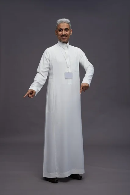 بورتريه لرجل عربي سعودي  خليجي يرتدي الثوب الابيض يقف و يقوم بايماءات واشارات مختلفه امام الكاميرا, خلفيه رماديه , كامل الجسم