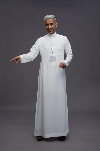 بورتريه لرجل عربي سعودي  خليجي يرتدي الثوب الابيض يقف و يقوم بايماءات واشارات مختلفه امام الكاميرا, خلفيه رماديه , كامل الجسم