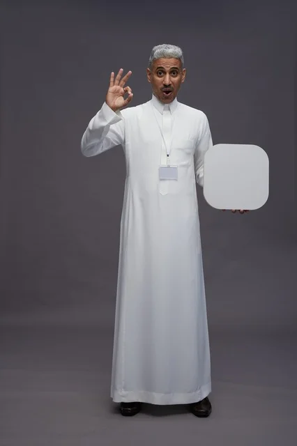 بورتريه لرجل عربي سعودي  خليجي يشير إلى لوح مربع ابيض فارغ , لوحه اعلانيه تسويقيه, كامل الجسم, خلفيه رماديه