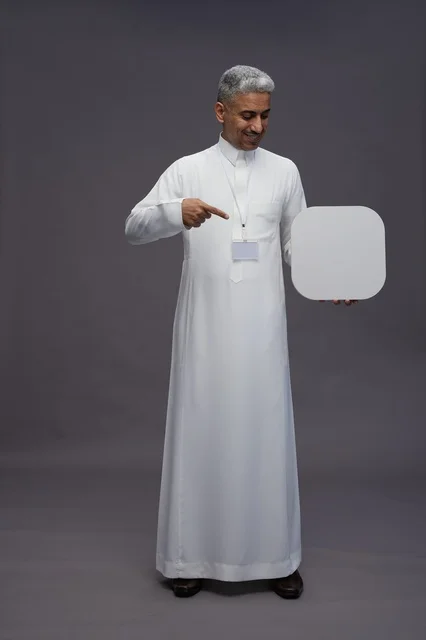 بورتريه لرجل عربي سعودي  خليجي يشير إلى لوح مربع ابيض فارغ , لوحه اعلانيه تسويقيه, كامل الجسم, خلفيه رماديه