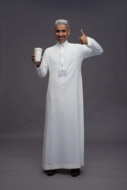 A portrait of an Arab Saudi Gulf man wearing a white thobe and enjoying drinking coffee, with a gray background, full body.