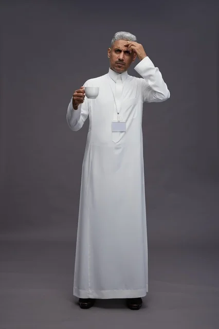 بورتريه لرجل عربي سعودي خليجي يرتدي الثوب الابيض ويستمتع بشرب القهوه, خلفيه رماديه, كامل الجسم