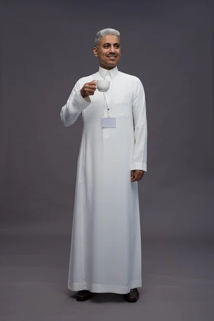 بورتريه لرجل عربي سعودي خليجي يرتدي الثوب الابيض ويستمتع بشرب القهوه, خلفيه رماديه, كامل الجسم