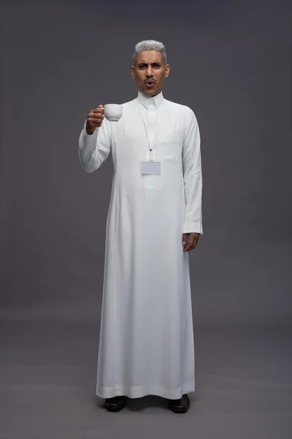 بورتريه لرجل عربي سعودي خليجي يرتدي الثوب الابيض ويستمتع بشرب القهوه, خلفيه رماديه, كامل الجسم