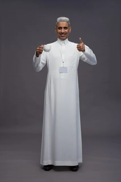 بورتريه لرجل عربي سعودي خليجي يرتدي الثوب الابيض ويستمتع بشرب القهوه, خلفيه رماديه, كامل الجسم