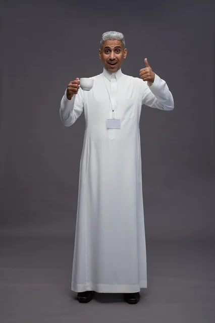 بورتريه لرجل عربي سعودي خليجي يرتدي الثوب الابيض ويستمتع بشرب القهوه, خلفيه رماديه, كامل الجسم