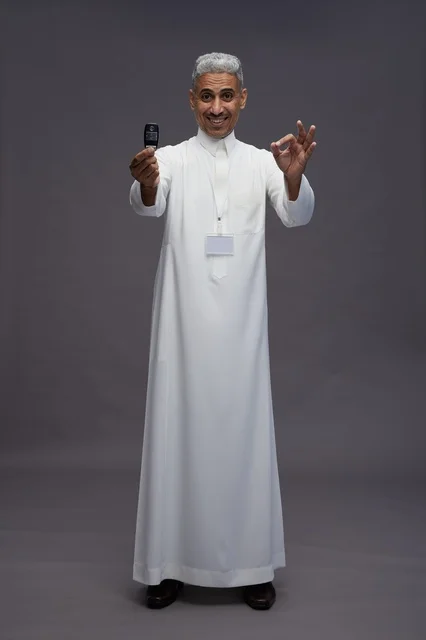 رجل عربي  سعودي  خليجي يرتدي الثوب الابيض يحمل مفتاح سيارة, مفهوم امتلاك سياره جديده, خلفيه رماديه