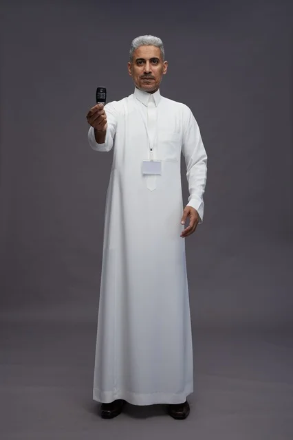 رجل عربي  سعودي  خليجي يرتدي الثوب الابيض يحمل مفتاح سيارة, مفهوم امتلاك سياره جديده, خلفيه رماديه