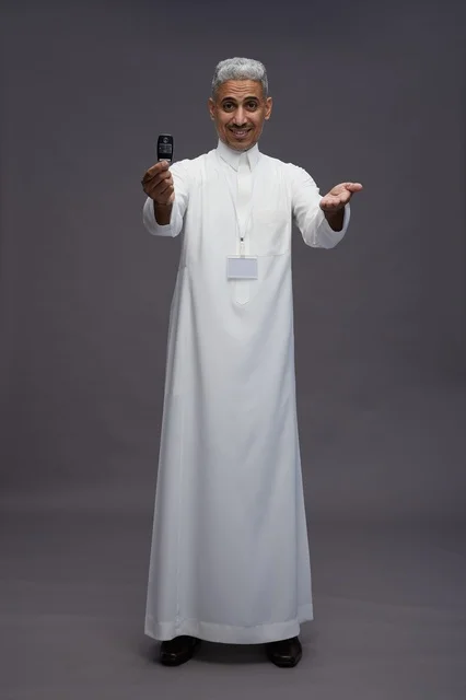 رجل عربي  سعودي  خليجي يرتدي الثوب الابيض يحمل مفتاح سيارة, مفهوم امتلاك سياره جديده, خلفيه رماديه