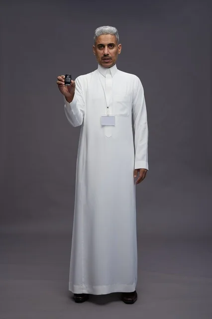 رجل عربي  سعودي  خليجي يرتدي الثوب الابيض يحمل مفتاح سيارة, مفهوم امتلاك سياره جديده, خلفيه رماديه