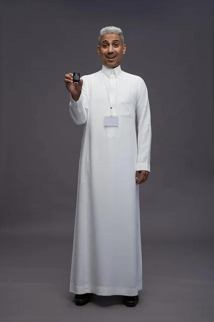 رجل عربي  سعودي  خليجي يرتدي الثوب الابيض يحمل مفتاح سيارة, مفهوم امتلاك سياره جديده, خلفيه رماديه