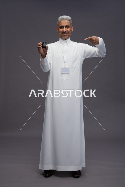 رجل عربي  سعودي  خليجي يرتدي الثوب الابيض يحمل مفتاح سيارة, مفهوم امتلاك سياره جديده, خلفيه رماديه