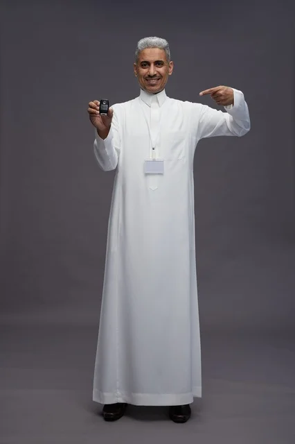 رجل عربي  سعودي  خليجي يرتدي الثوب الابيض يحمل مفتاح سيارة, مفهوم امتلاك سياره جديده, خلفيه رماديه