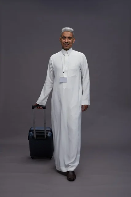 Portrait of a Saudi Arabian Gulf man standing with a suitcase, concept of tourism and travel, gray background, full body.