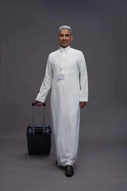 Portrait of a Saudi Arabian Gulf man standing with a suitcase, concept of tourism and travel, gray background, full body.