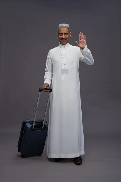 Portrait of a Saudi Arabian Gulf man standing with a suitcase, concept of tourism and travel, gray background, full body.