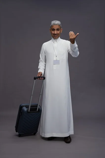 Portrait of a Saudi Arabian Gulf man standing with a suitcase, concept of tourism and travel, gray background, full body.