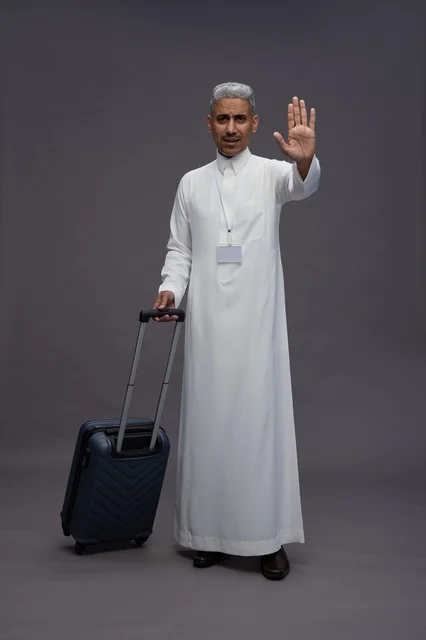 Portrait of a Saudi Arabian Gulf man standing with a suitcase, concept of tourism and travel, gray background, full body.