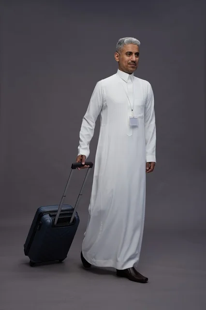 Portrait of a Saudi Arabian Gulf man standing with a suitcase, concept of tourism and travel, gray background, full body. Portrait of a Saudi Arabian Gulf man standing with a suitcase, concept of tourism and travel, gray background, full body.