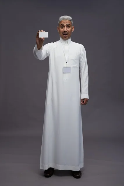 بورتريه لرجل عربي سعودي خليجي يرتدي الثوب الابيض يعرض بطاقة ائتمان بيضاء فارغه ويشير اليها, كرت تعريفي شخصي, الجسم بالكامل, خلفيه رماديه