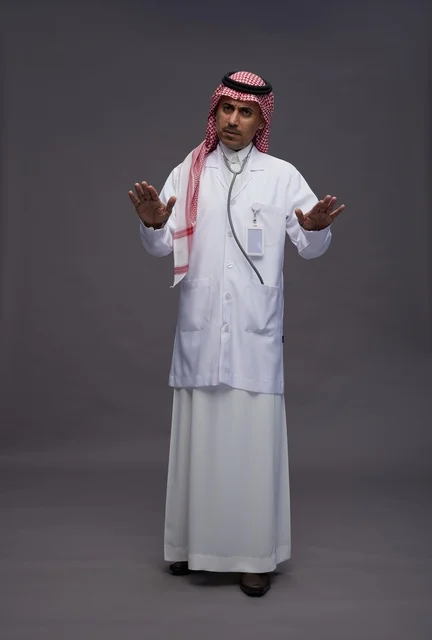 طبيب عربي سعودي خليجي يرتدي الثوب والمعطف الابيض مع سماعة الطب يقوم بايماءات واشارات مختلفه, كامل الجسم, خلفيه رماديه