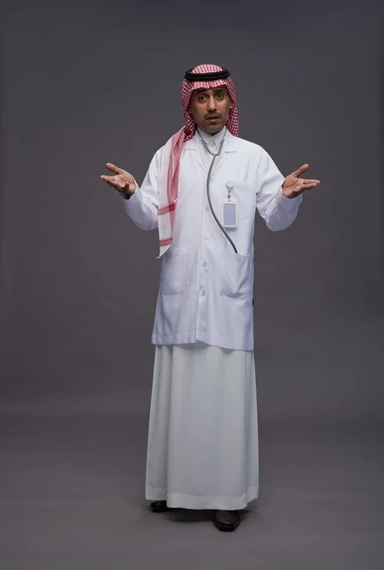 طبيب عربي سعودي خليجي يرتدي الثوب والمعطف الابيض مع سماعة الطب يقوم بايماءات واشارات مختلفه, كامل الجسم, خلفيه رماديه