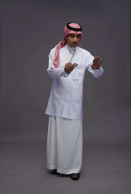 طبيب عربي سعودي خليجي يرتدي الثوب والمعطف الابيض مع سماعة الطب يقوم بايماءات واشارات مختلفه, كامل الجسم, خلفيه رماديه