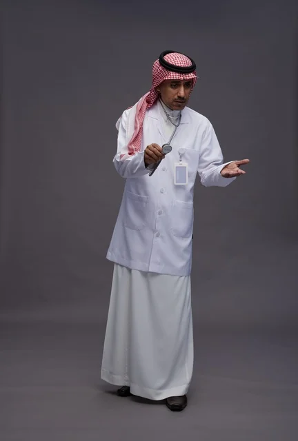 طبيب عربي سعودي خليجي يرتدي الثوب والمعطف الابيض مع سماعة الطب يقوم بايماءات واشارات مختلفه, كامل الجسم, خلفيه رماديه