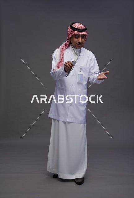 طبيب عربي سعودي خليجي يرتدي الثوب والمعطف الابيض مع سماعة الطب يقوم بايماءات واشارات مختلفه, كامل الجسم, خلفيه رماديه