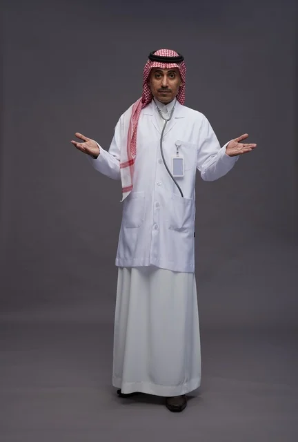طبيب عربي سعودي خليجي يرتدي الثوب والمعطف الابيض مع سماعة الطب يقوم بايماءات واشارات مختلفه, كامل الجسم, خلفيه رماديه