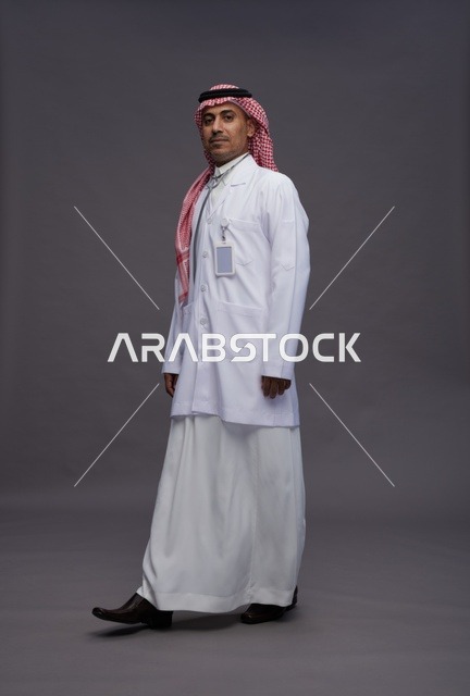 طبيب عربي سعودي خليجي يرتدي الثوب والمعطف الابيض مع سماعة الطب يقوم بايماءات واشارات مختلفه, كامل الجسم, خلفيه رماديه