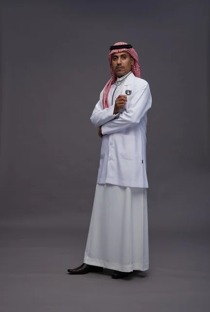 طبيب عربي سعودي خليجي يرتدي الثوب والمعطف الابيض مع سماعة الطب يقوم بايماءات واشارات مختلفه, كامل الجسم, خلفيه رماديه