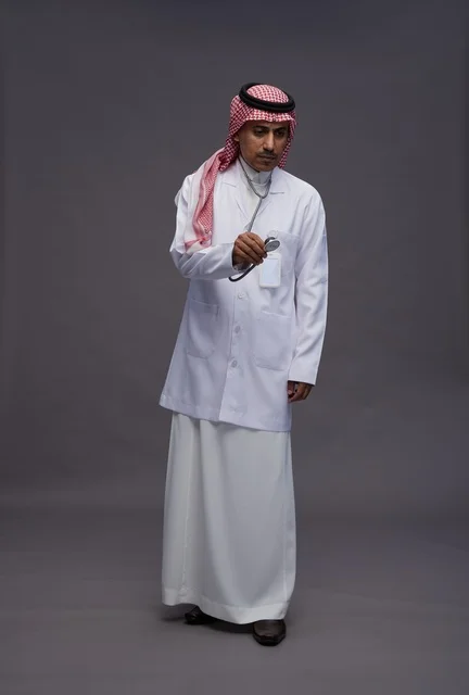 طبيب عربي سعودي خليجي يرتدي الثوب والمعطف الابيض مع سماعة الطب يقوم بايماءات واشارات مختلفه, كامل الجسم, خلفيه رماديه