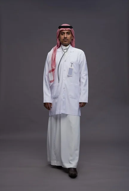 طبيب عربي سعودي خليجي يرتدي الثوب والمعطف الابيض مع سماعة الطب يقوم بايماءات واشارات مختلفه, كامل الجسم, خلفيه رماديه
