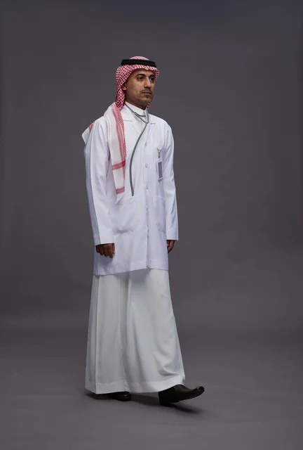 طبيب عربي سعودي خليجي يرتدي الثوب والمعطف الابيض مع سماعة الطب يقوم بايماءات واشارات مختلفه, كامل الجسم, خلفيه رماديه